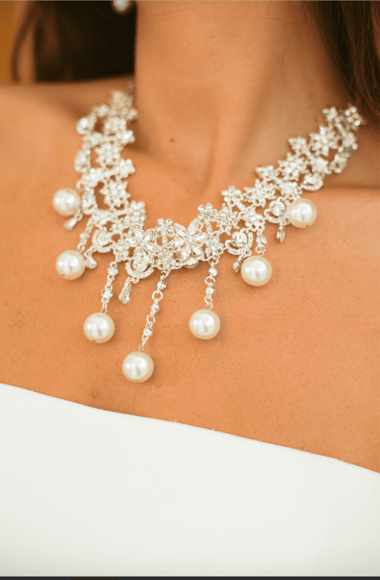 Close-up of a pearl and crystal necklace on a person wearing a white dress.