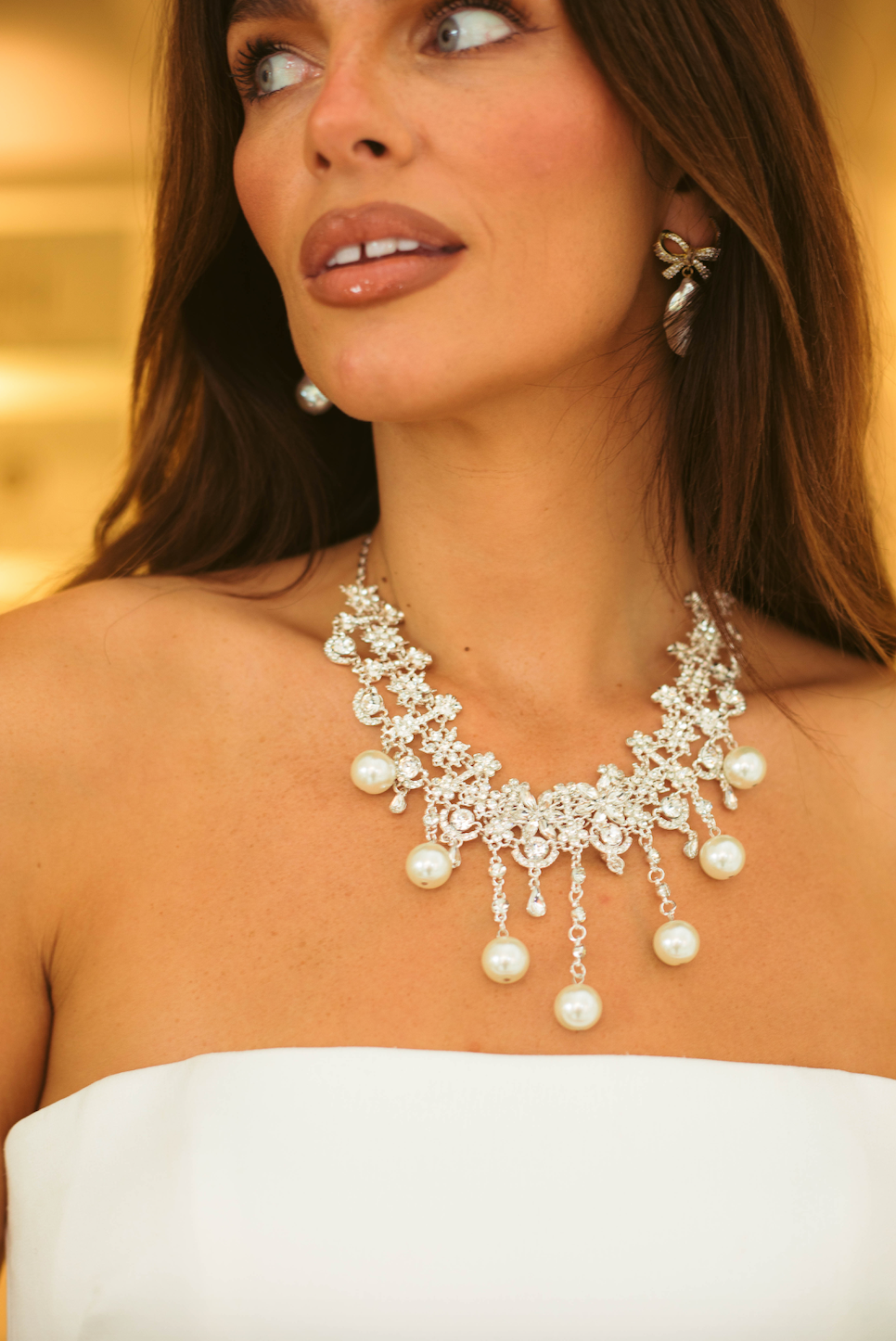 Woman wearing a sparkling diamante necklace with pearls against a warm-toned background